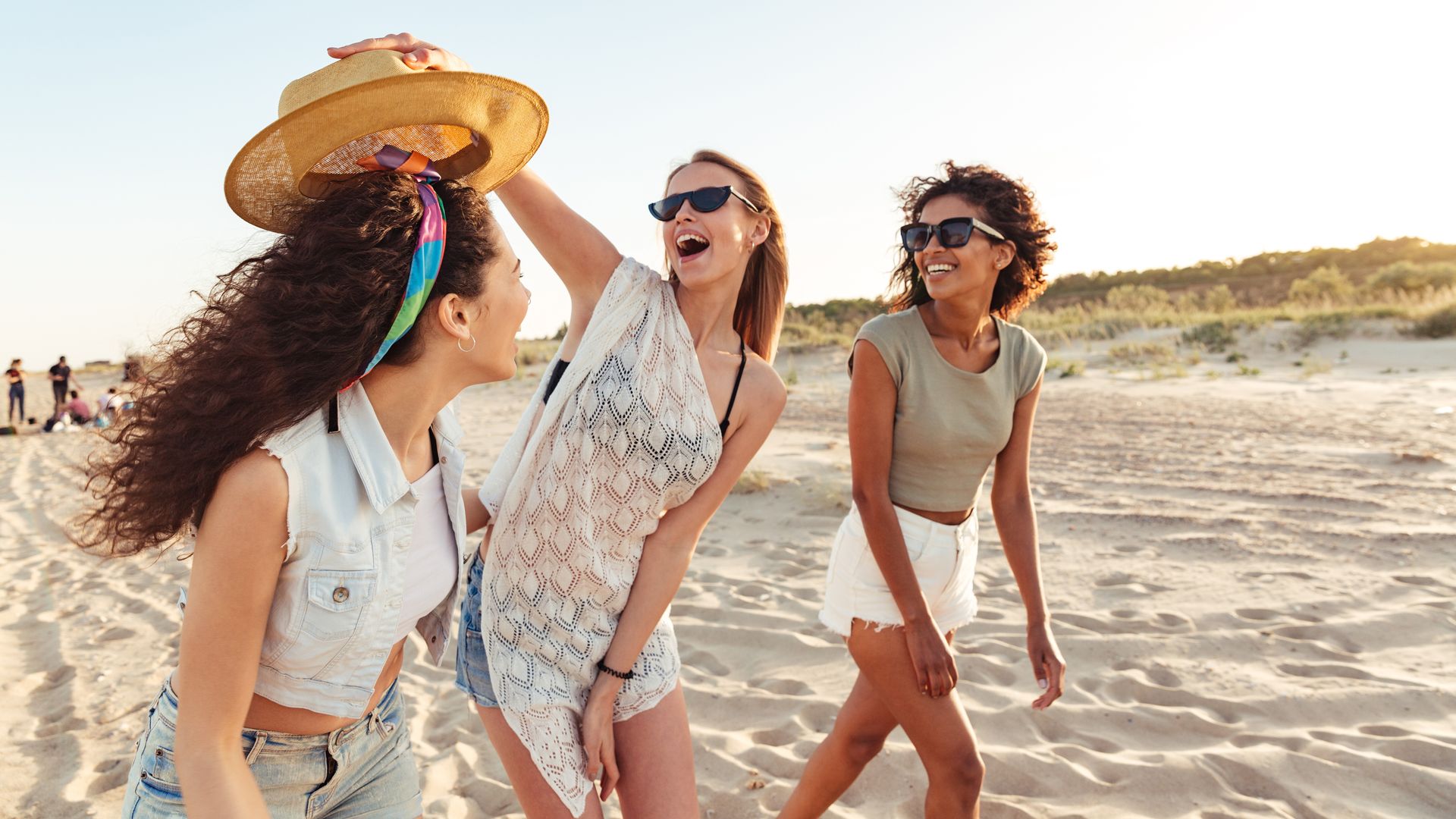 tres amigas felices y sonrientes en la arena de la playa