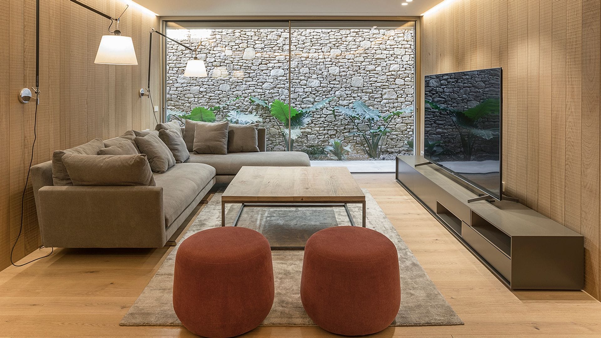 Salón con paredes y suelo de madera, mueble de televisión, sofá rinconera y dos puffs