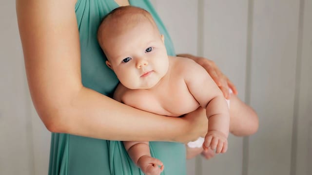Madre sostiene a su bebé en su brazo para aliviar los gases