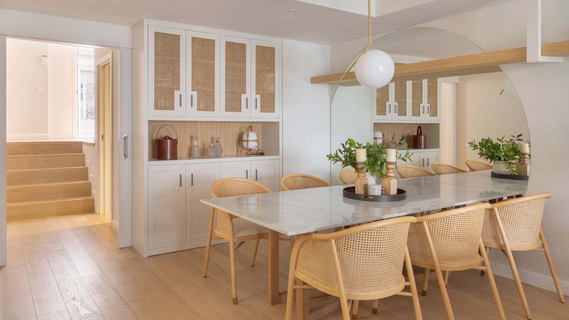 Comedor con mesa rectangular, mueble a medida con puertas de vitrina, sillas de rejilla, lámpara de techo blanca