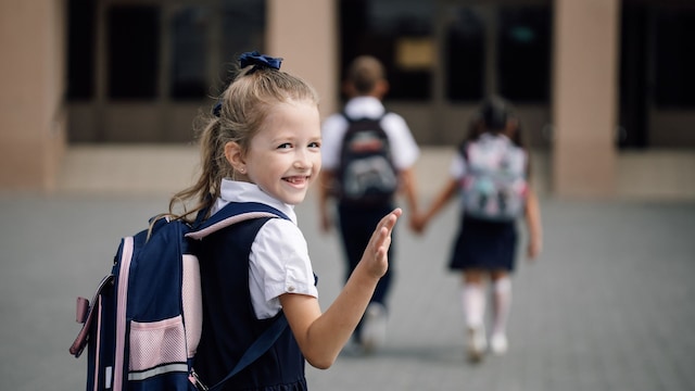 Niña de uniforme sonríe al despedirse para entrar en el colegio