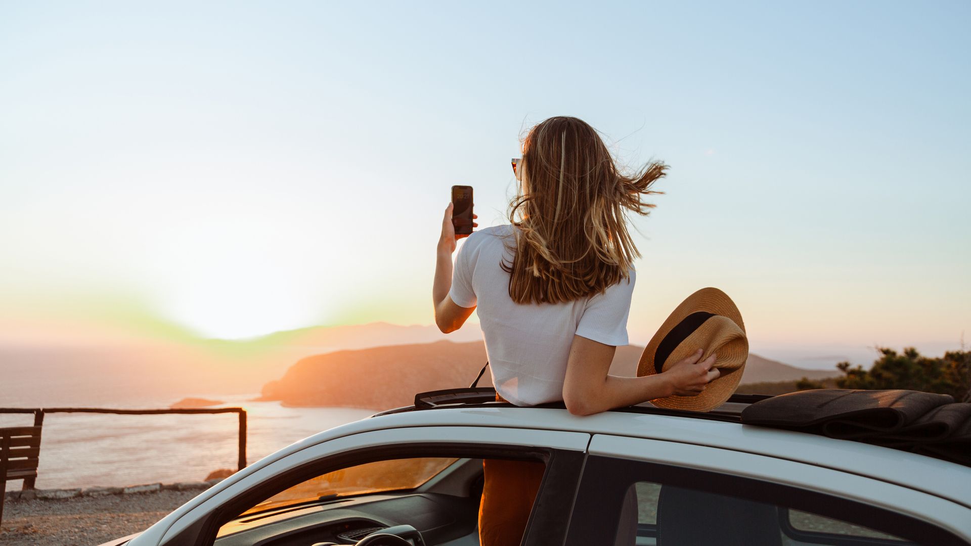 Mujer tomando una foto desde su coche en un paisaje idílico de vacaciones durante el verano y al atardecer