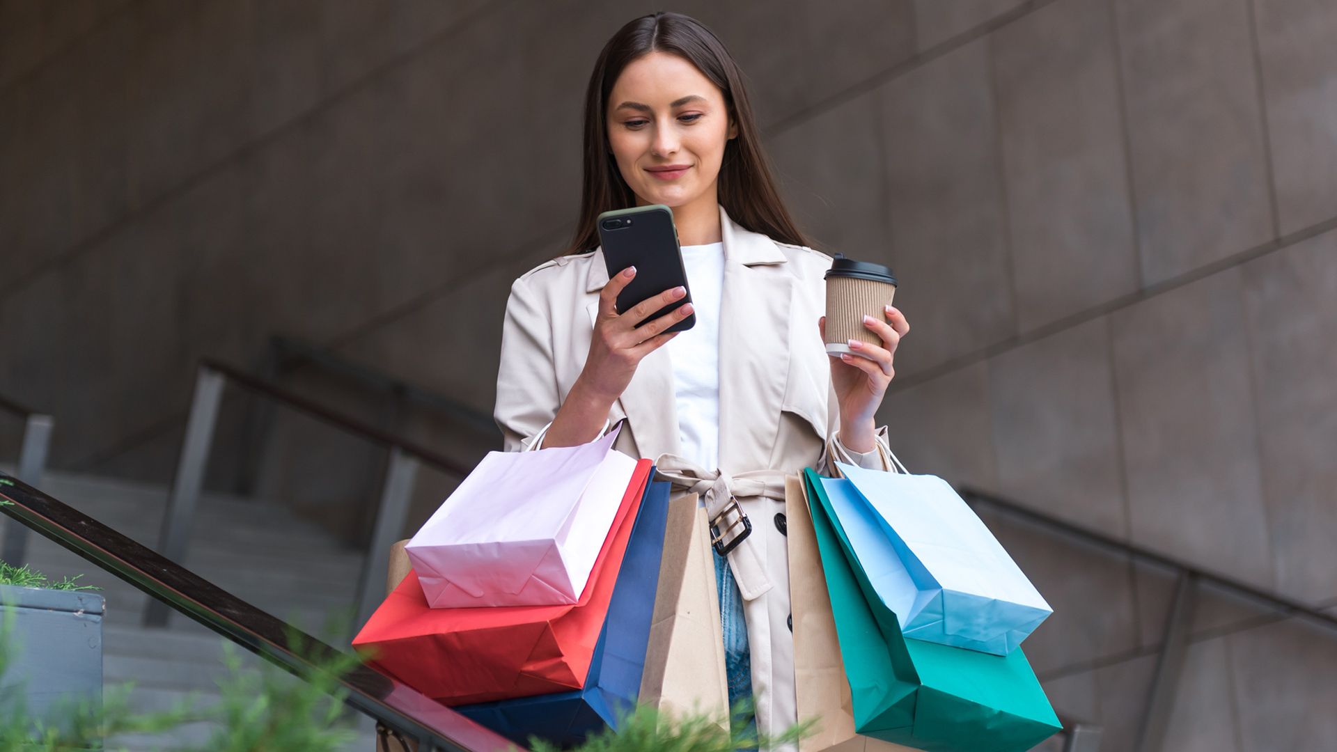 Mujer en la calle con bolsas de compras, café y teléfono móvil