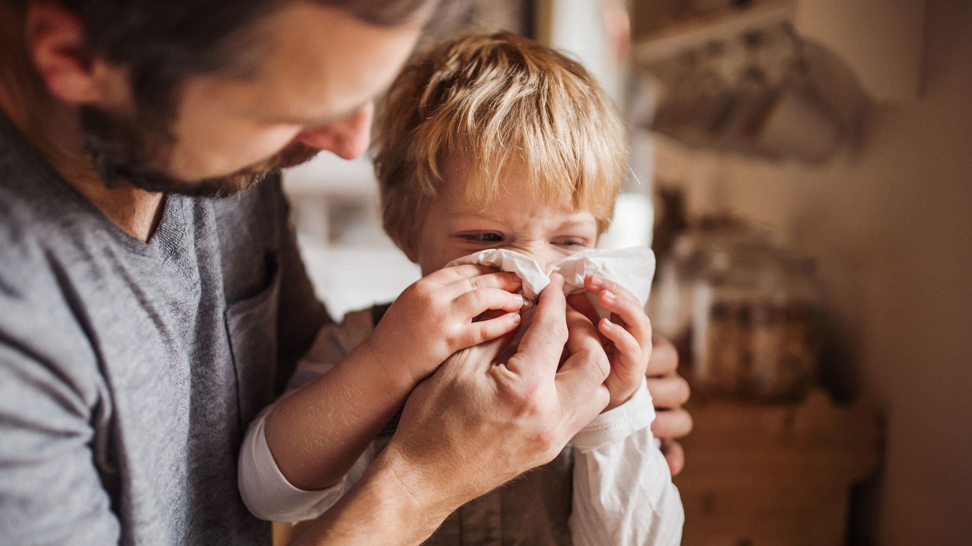 Padre ayuda a sonarse a su hijo, un niño pequeño con gripe