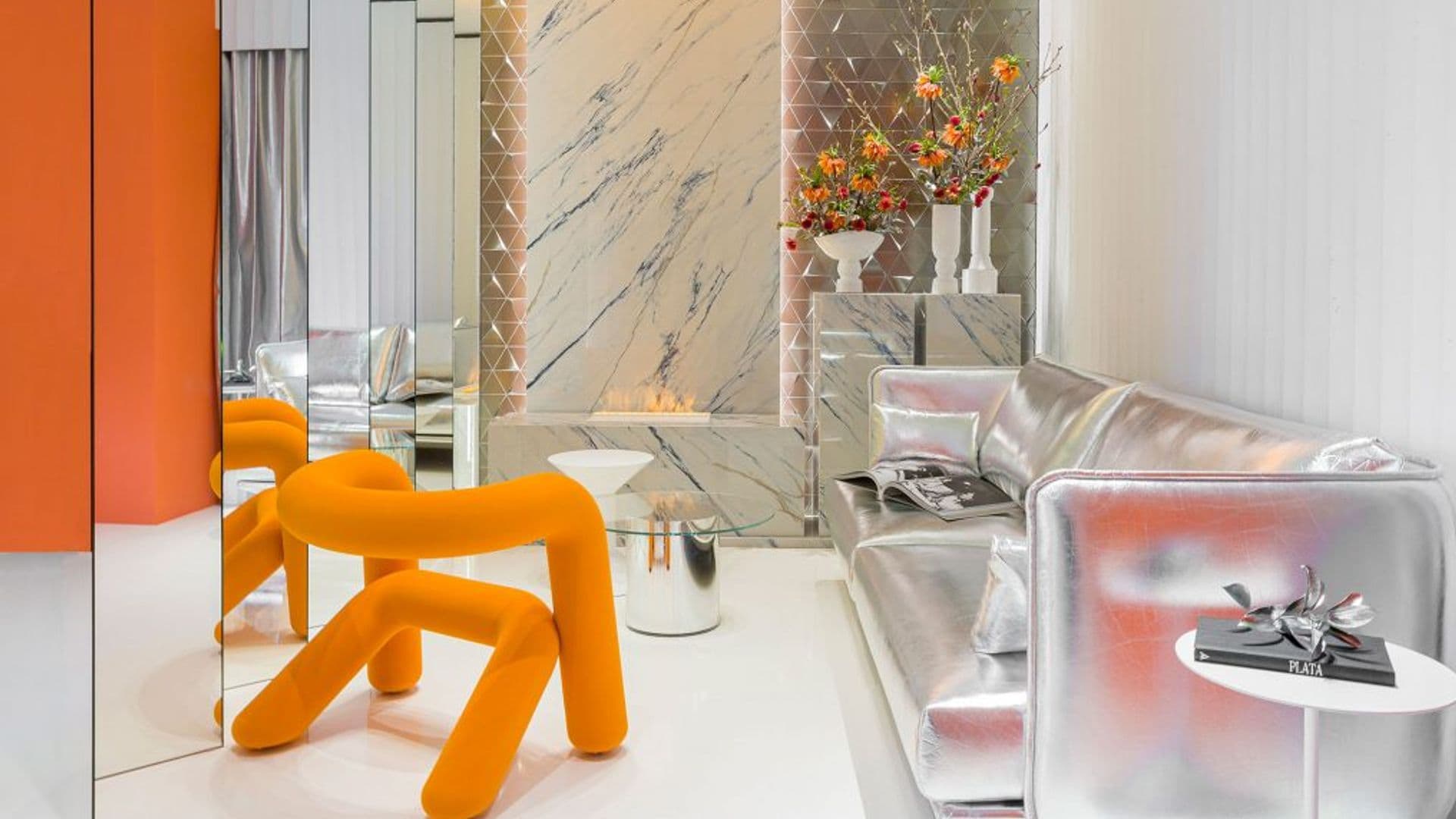 Salón de estilo futurista con sofá plateado, silla naranja y espejos 