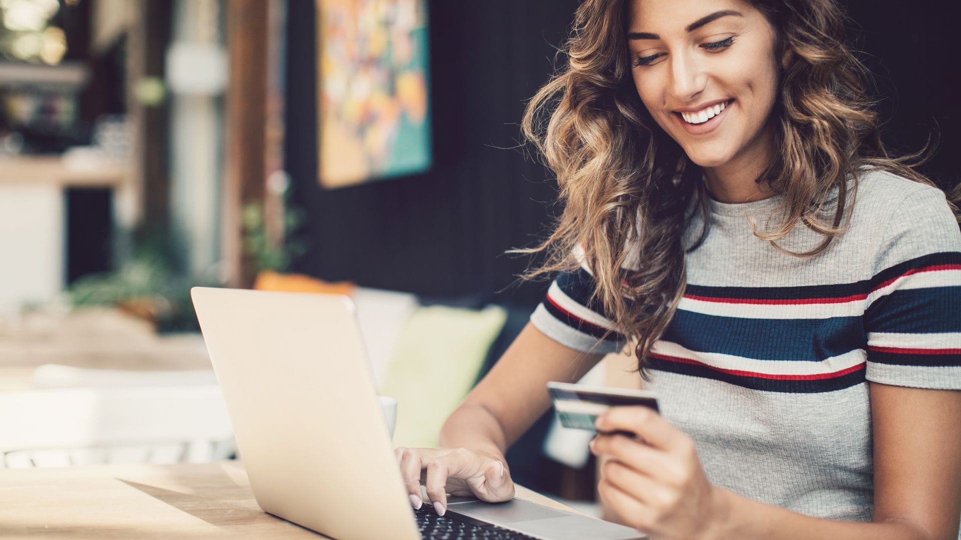 Smiling young woman holding a credit card and typing on a laptop.