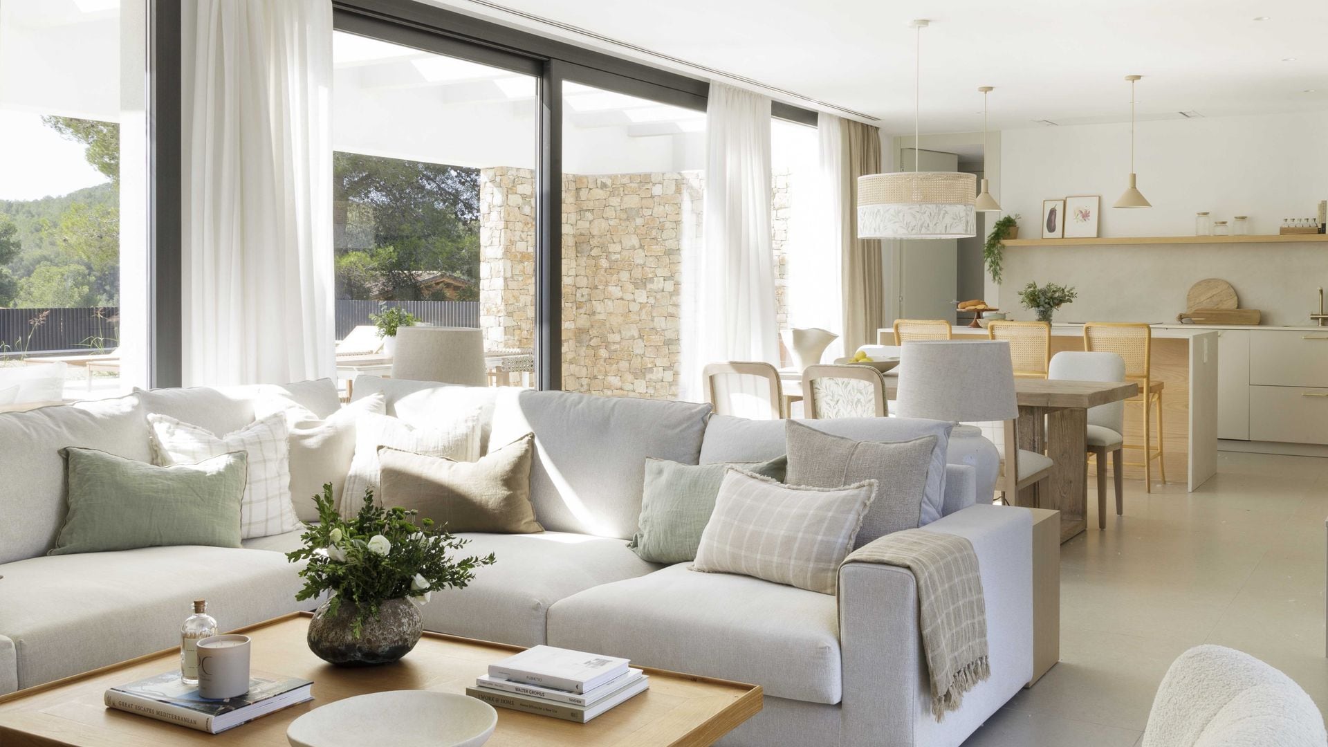 Salón comedor y cocina en tonos claros, con grandes ventanales con cortinas y visillos en blanco y beige