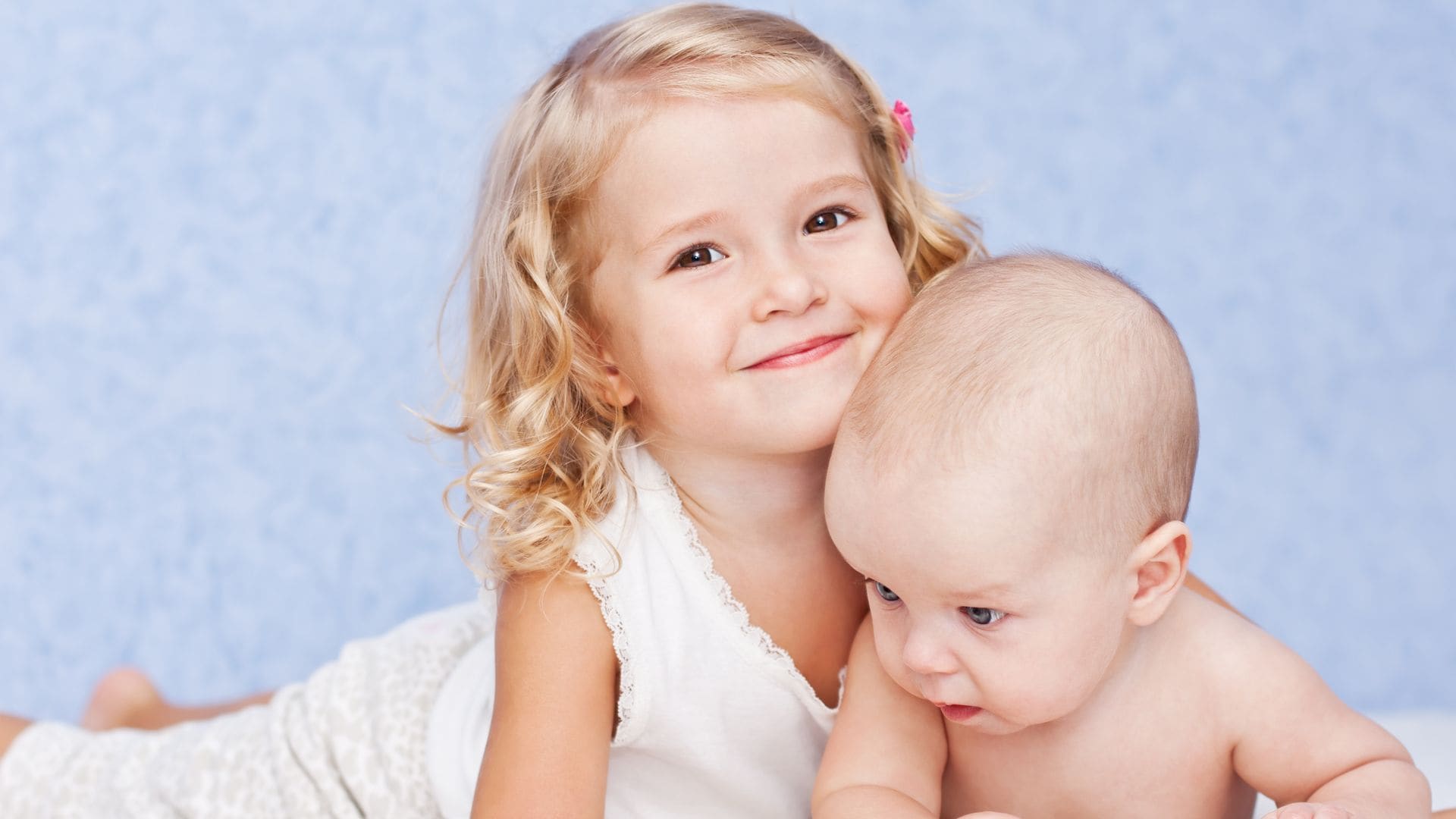 Niña rubia, junto a su hermanito, sonríe