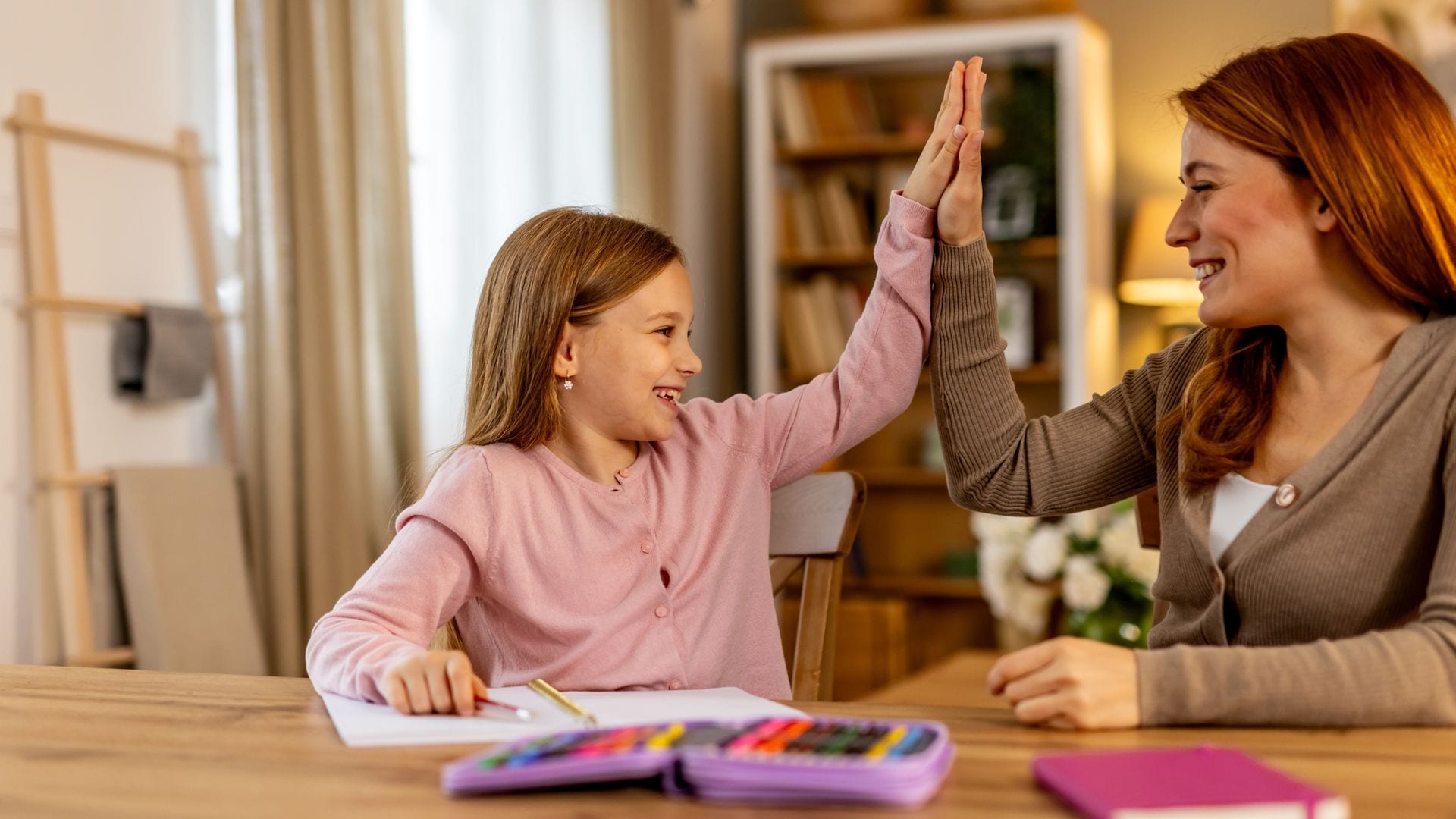 Madre choca los cinco con su hija, que está haciendo los deberes