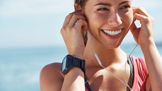 Una joven alegre poniéndose los auriculares antes de una sesión de carrera