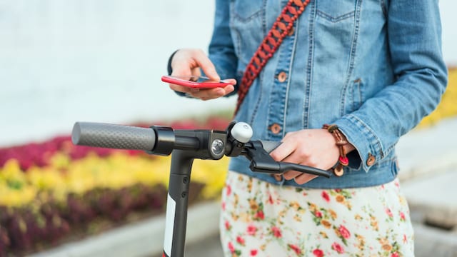 Una chica con su móvil junto a un patinete eléctrico