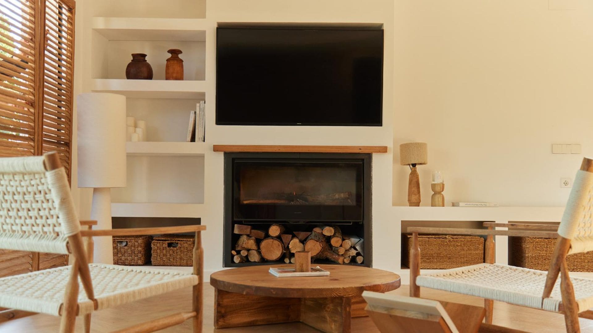 Salón con chimenea y televisión en la pared con butacas de fibras vegetales y mesa de centro de madera