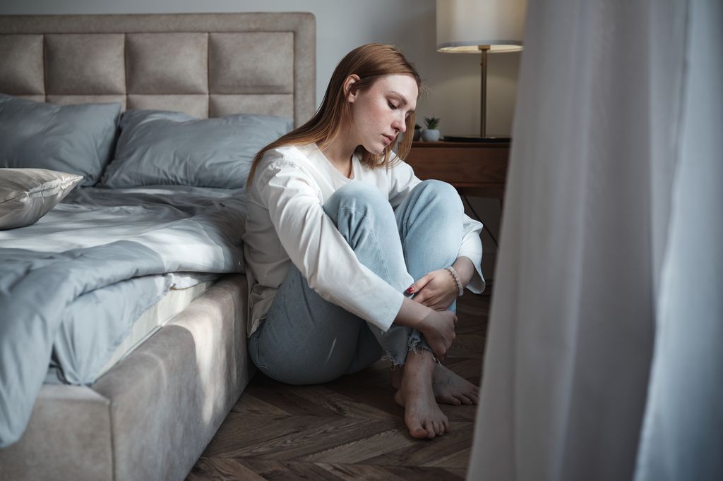 mujer triste sentada en el suelo, junto a la cama