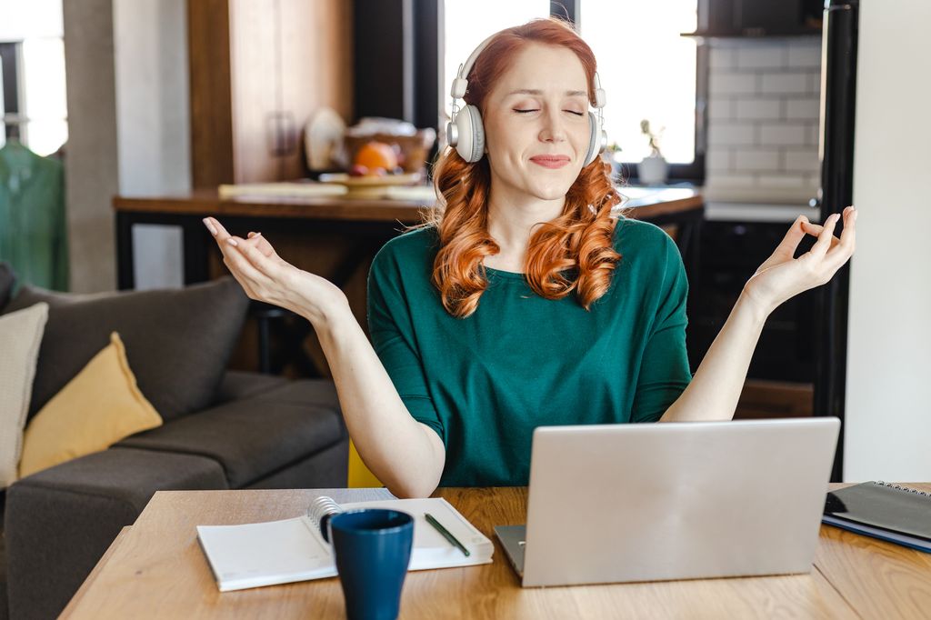 mujer meditando relajada con unos cascos frente a su ordenador