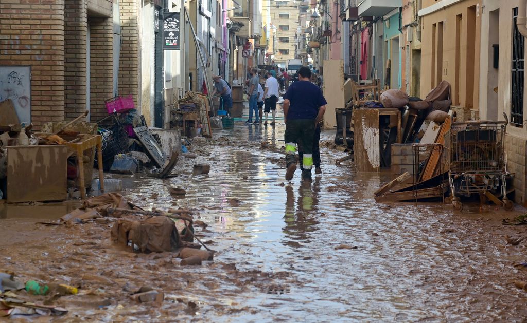 Residents try to clean their houses as the street is covered in mud on October 31, 2024 after flash floods affected the town of Alfafar, in the region of Valencia, eastern Spain. Rescuers raced on October 31, 2024 to find survivors and victims of once-in-a-generation floods in Spain that killed at least 95 people and left towns submerged in a muddy deluge with overturned cars scattered in the streets. About 1,000 troops joined police and firefighters in the grim search for bodies in the Valencia region as Spain started three days of mourning. Up to a year's rain fell in a few hours on the eastern city of Valencia and surrounding region on October 29 sending torrents of water and mud through towns and cities. (Photo by JOSE JORDAN / AFP) (Photo by JOSE JORDAN/AFP via Getty Images)