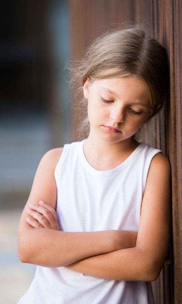 Niña triste apoyada en pared