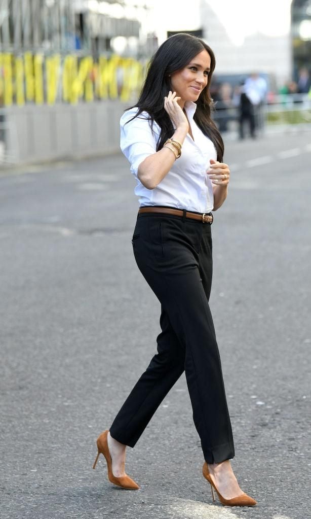 Meghan Makle camina con look de camisa blanca, pantalón negro y pumps marrones