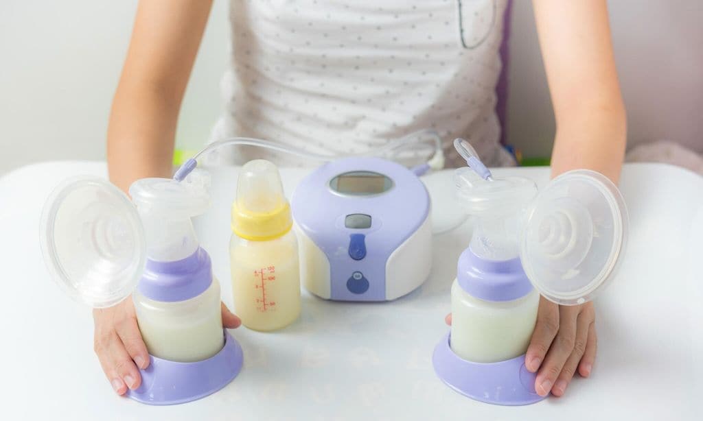 manos de mujer con extractor de leche y botellas llenas de leche materna sobre una mesa