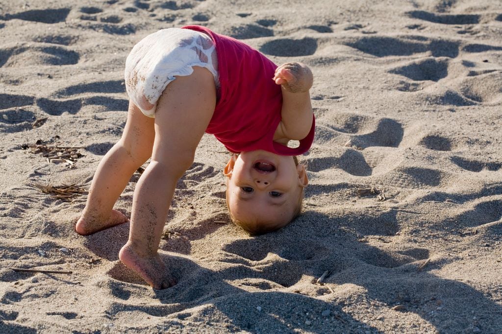 Bebé cabeza abajo sobre la arena de la playa