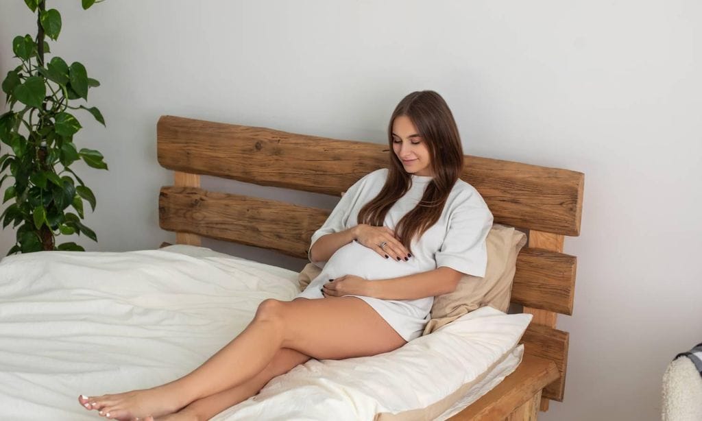 mujer embarazada tumbada sobre la cama mientras se abraza la tripa