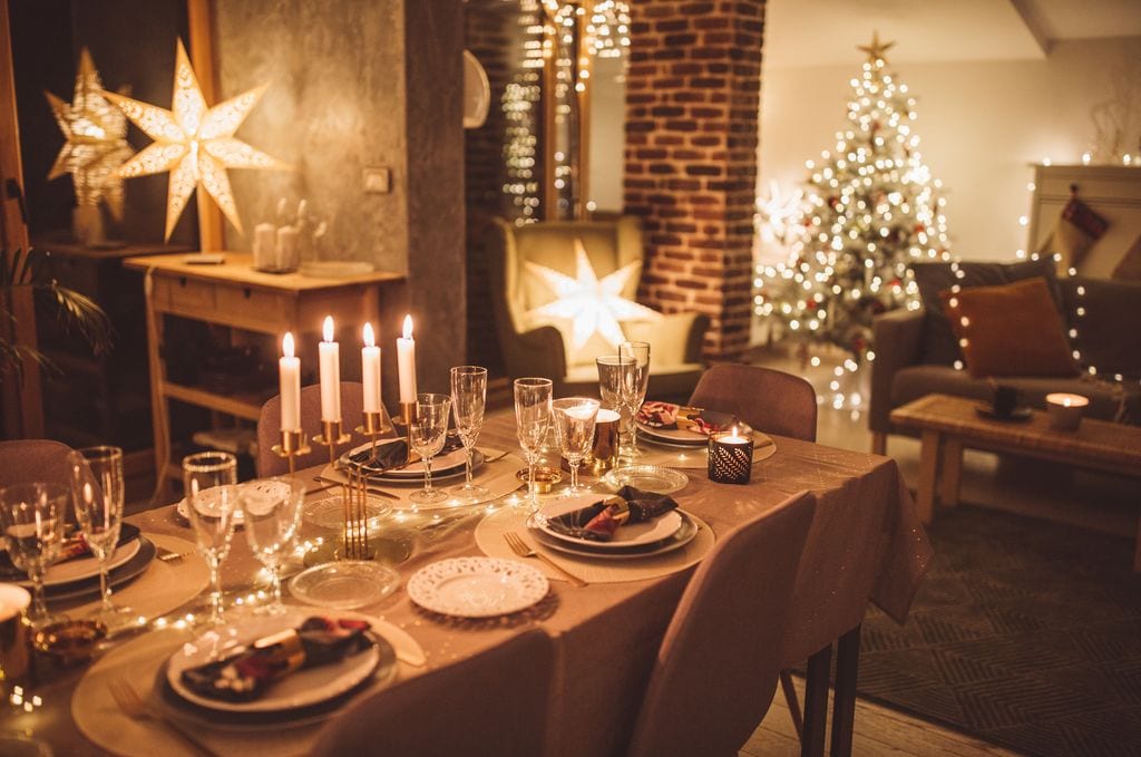 Mesa preparada para la cena de Navidad, iluminada con velas. Casa adornada con luces de Navidad