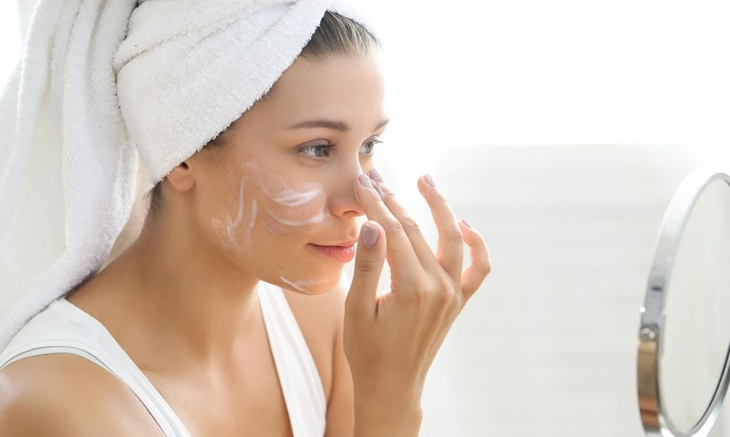 Mujer aplicando crema en su rostro frente a un espejo