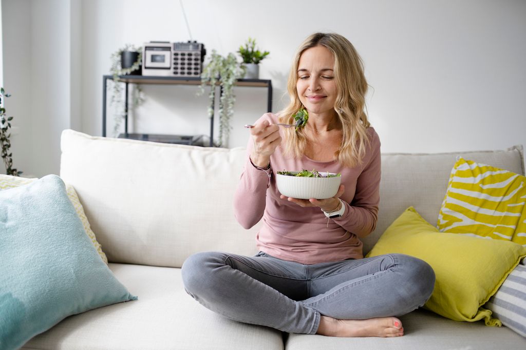 mujer comiendo ensalada sentada en el sofá