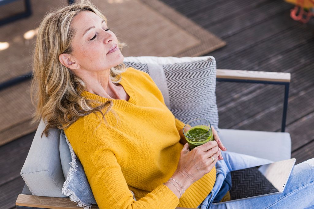 Retrato de una mujer madura sentada en la terraza con una tableta digital y un vaso de batido