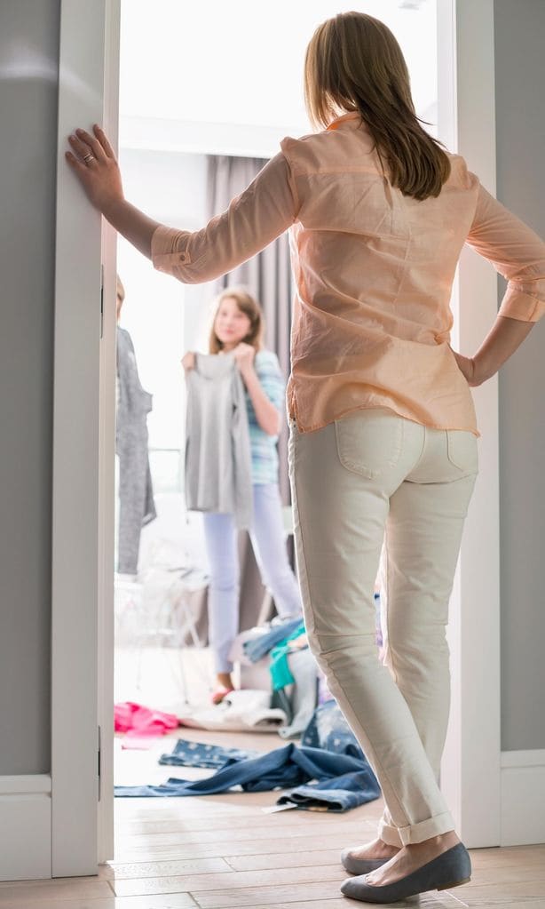 Madre mirando a su hija cómo se prueba ropa en su habitación