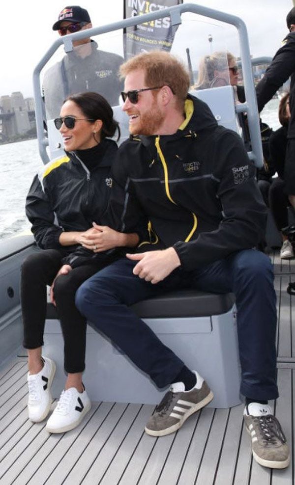 Meghan Markle con zapatos deportivos Veja, atuendo negro y gafas de sol junto al príncipe Harry