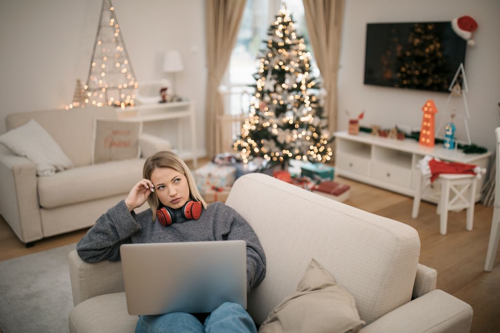 mujer preocupada mirando su portátil con la casa decorada en Navidad