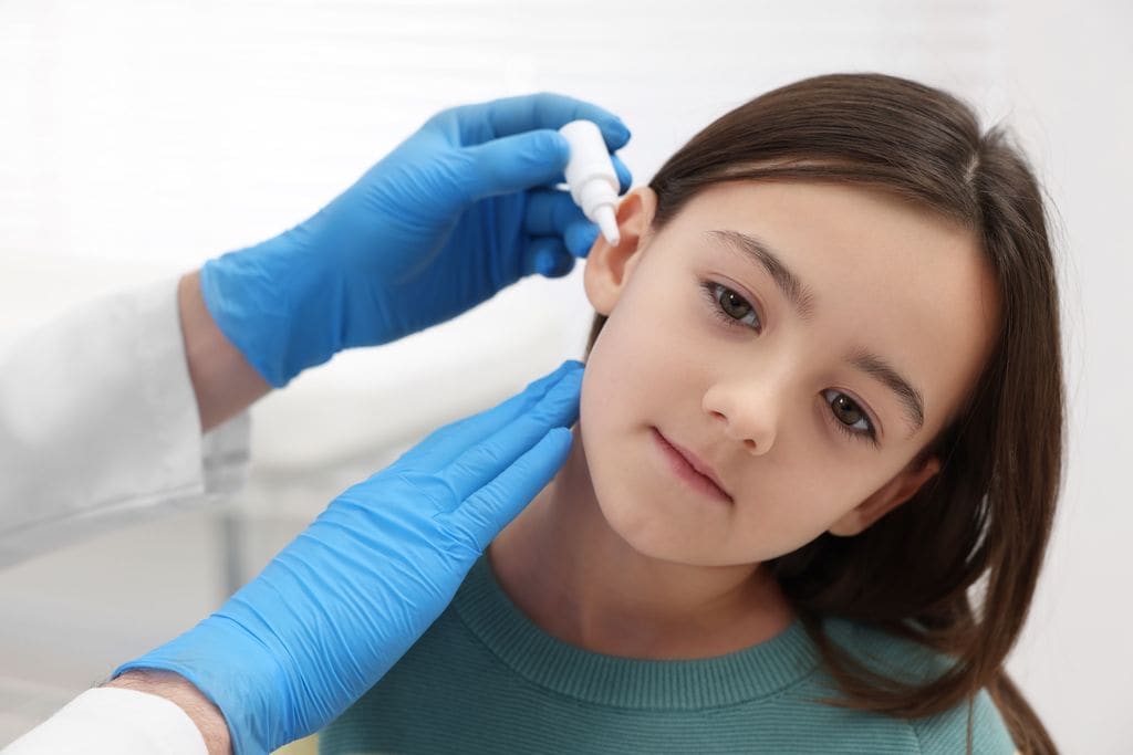 Médico poniendo gotas en el oído a una niña con otitis