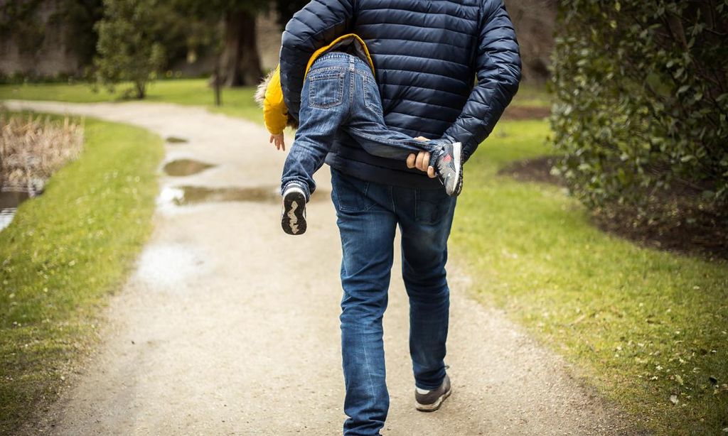 padre llevando en brazos a su hijo por el parque