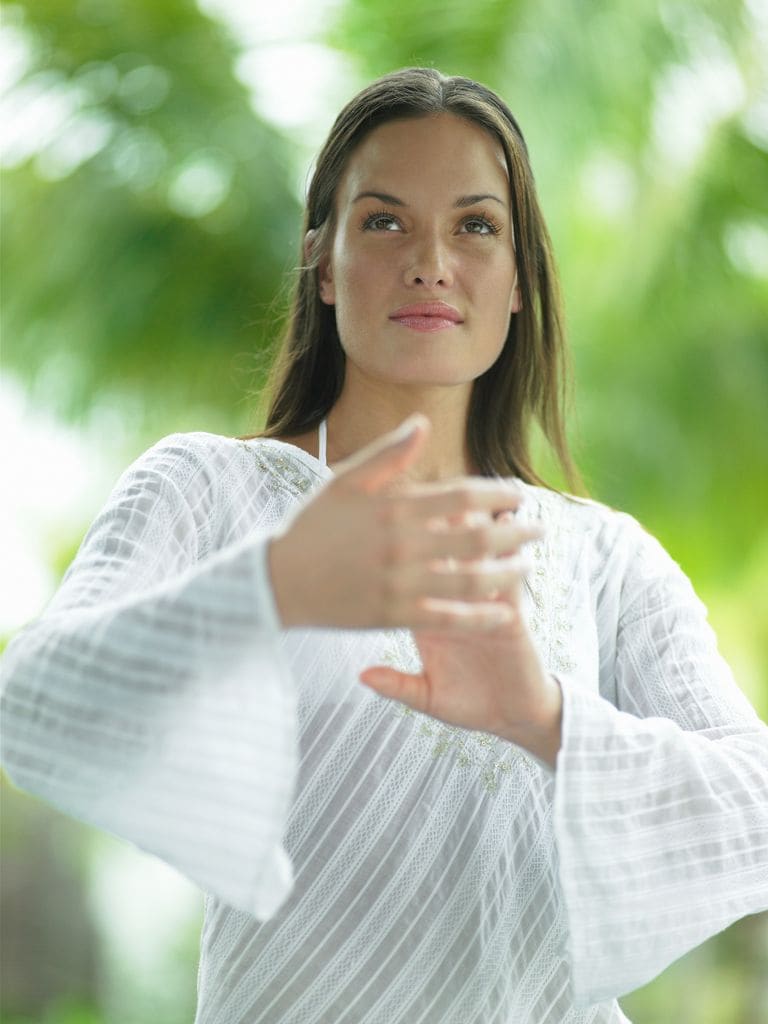 Mujer vestida de blanco practicando Taichi en la naturaleza