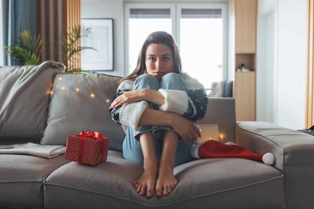 mujer triste y pensativa sentada en el sofá en Navidad