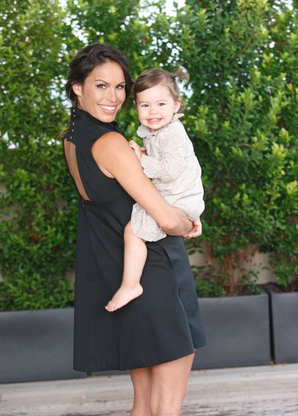 Mireia Canalda, con vestido negro de Alex Vidal, sujeta en brazos a su hija, Inés con vestido camel estampado de Neck & Neck © ¡HOLA!