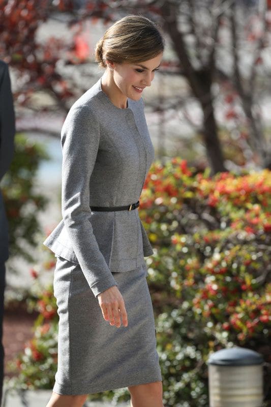 Doña Letizia con un conjunto gris, y al igual que su homóloga jordana, zapatos negros, en su caso de Prada, y bolso de mano de Hugo Boss y unos originales pendientes de estilo 'ear-cuff' con forma de pluma
