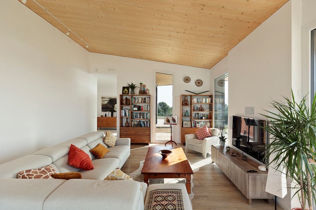 Salón con sofás blancos, librerías de madera, techo de madera, sillón, mueble de televisión, mesa de centro de madera