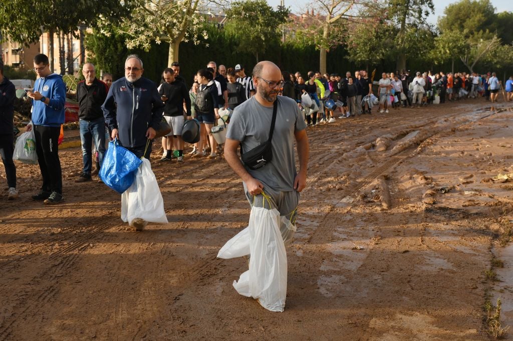 VALENCIA, SPAIN - OCTOBER 31: Men walk through mud with bags over their feet as people line up to collect water from a broken pipe after flooding hit large parts of the country on October 31, 2024 in the Paiporta municipality of Valencia, Spain. By Thursday, Spanish authorities confirmed that at least 95 people had died, mostly in the Valencia region, amid the flooding that swept eastern and southern parts of the country starting on Tuesday. The intense rainfall event is known as a "cold drop" or DANA weather system. (Photo by David Ramos/Getty Images)