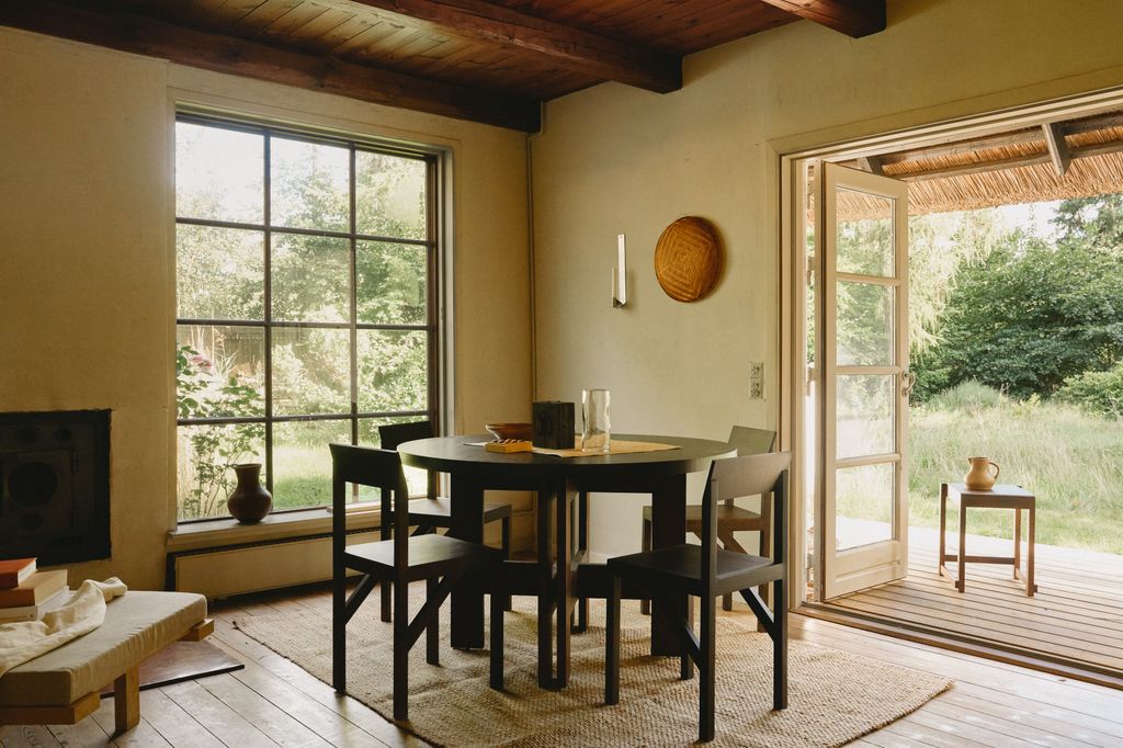 Comedor con salida al jardín con gran ventanal, vigas de madera en el techo, comedor con muebles negros y mesa redonda 