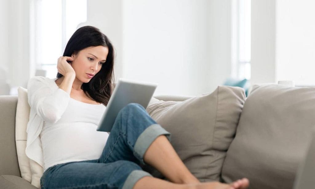 mujer embarazada tumbada en sof mirando tablet