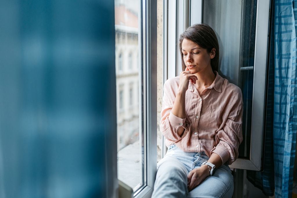 mujer pensativa y seria sentada junto a la ventana