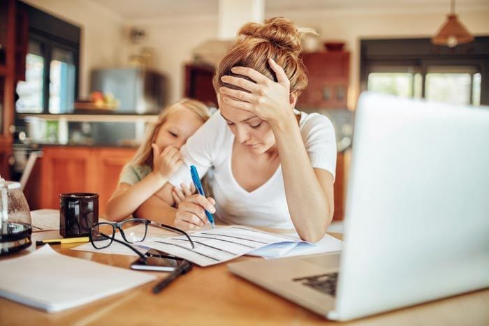 mujer agobiada frente al ordenador con su hija al lado