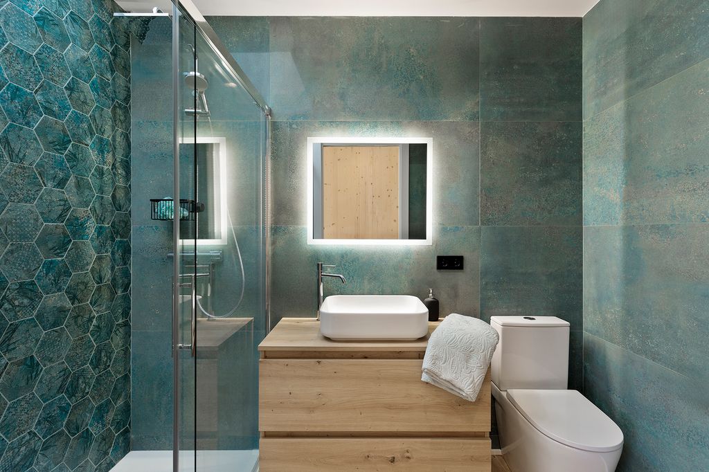 Baño con ducha, revestido de azulejos en color azul, espejo retroiluminado, mueble bajolavabo de madera