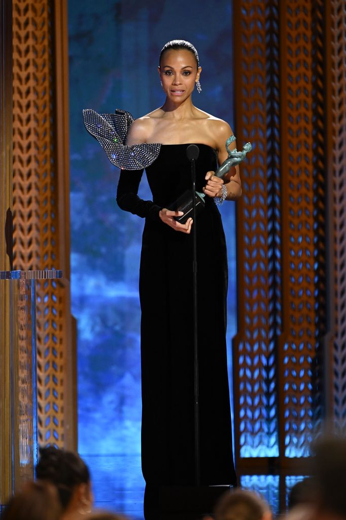 Zoe Saldaña en el escenario sosteniendo su premio SAG Award, vestida elegantemente de negro, durante la ceremonia de premiación.