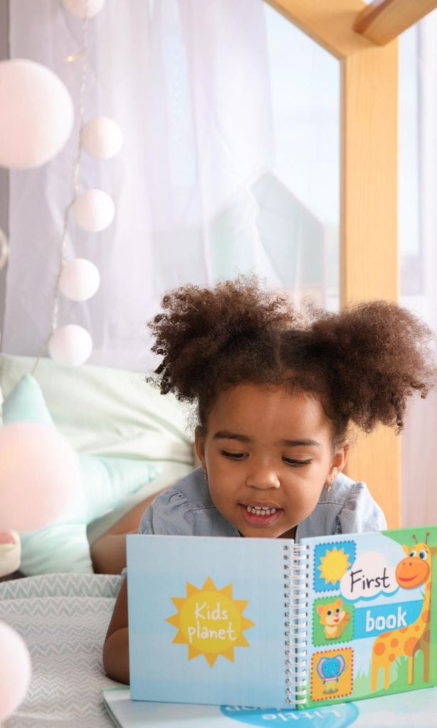 Niña leyendo cuento feliz tumbada en el suelo