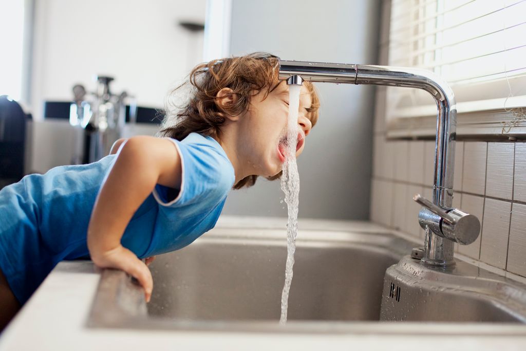 Un niño bebiendo agua de un grifo