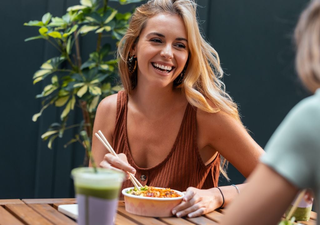 Dos mujeres comiendo en una terraza comiendo poke y un batido verde