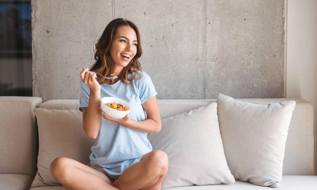 mujer comiendo un plato saludable sentada en el sof 