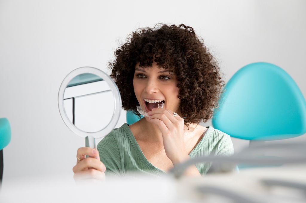 mujer frente al espejo, colocándose una férula o un alineador dental